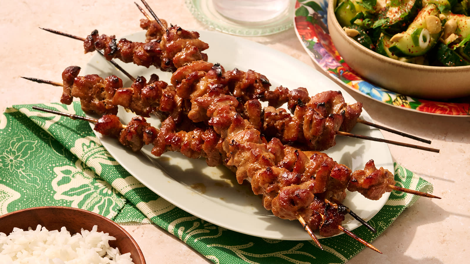 Filippinske grillspyd med agurksalat servert på hvitt ovalt fat. Skåler med agurksalat og ris på siden.