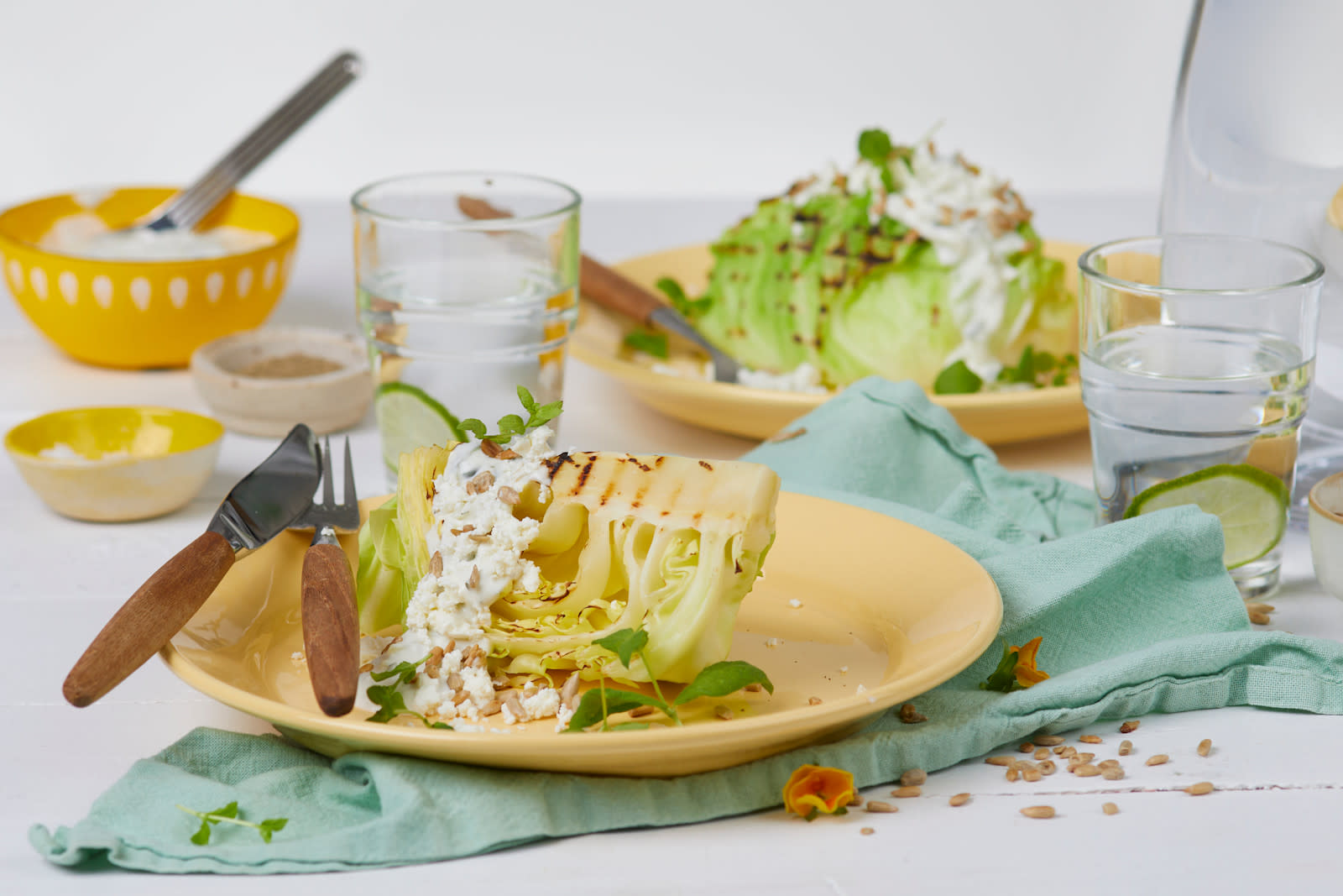 Nykål med feta og tzatziki på en gul tallerken oppå en blå serviett. Dette er foran en gul skål med tzatziki og en gul tallerken med kål.