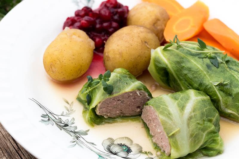 Hjemmelagede kålruletter servert på lys middagstallerken, med kokt potet, gulrot og tyttebær på siden.