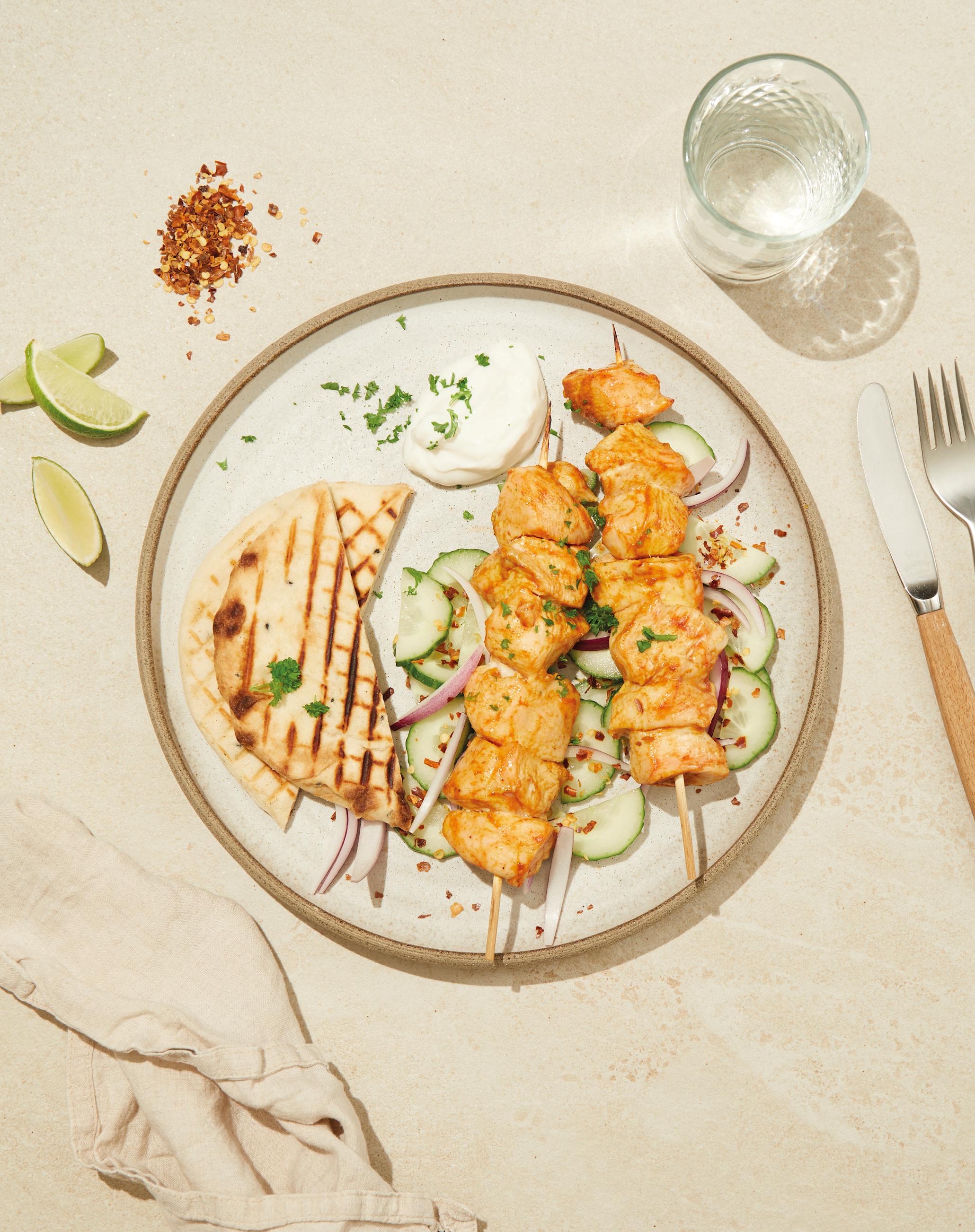 Yoghurtmarinert indisk kylling, med agurkskiver, rødløk og pitabrød, på tallerken