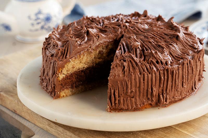 Tropisk aroma dekket med sjokoladesmørkrem, med et stykke av kaken skåret ut så man ser den tofargede innsiden. Kaken er servert på rundt marmorfat.