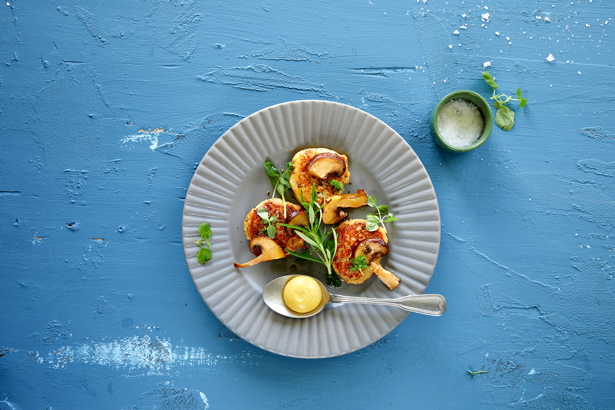 Fiskekaker med sopp og gressløk, servert på grå tallerken, med hjemmelaget dip. Blå bakgrunn.