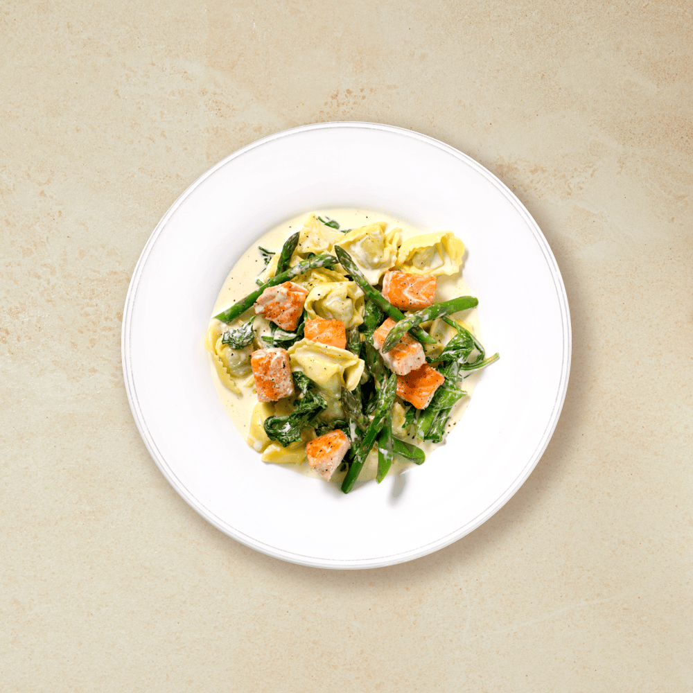 Tortellini med laks og grønnsaker, servert på en hvit tallerken