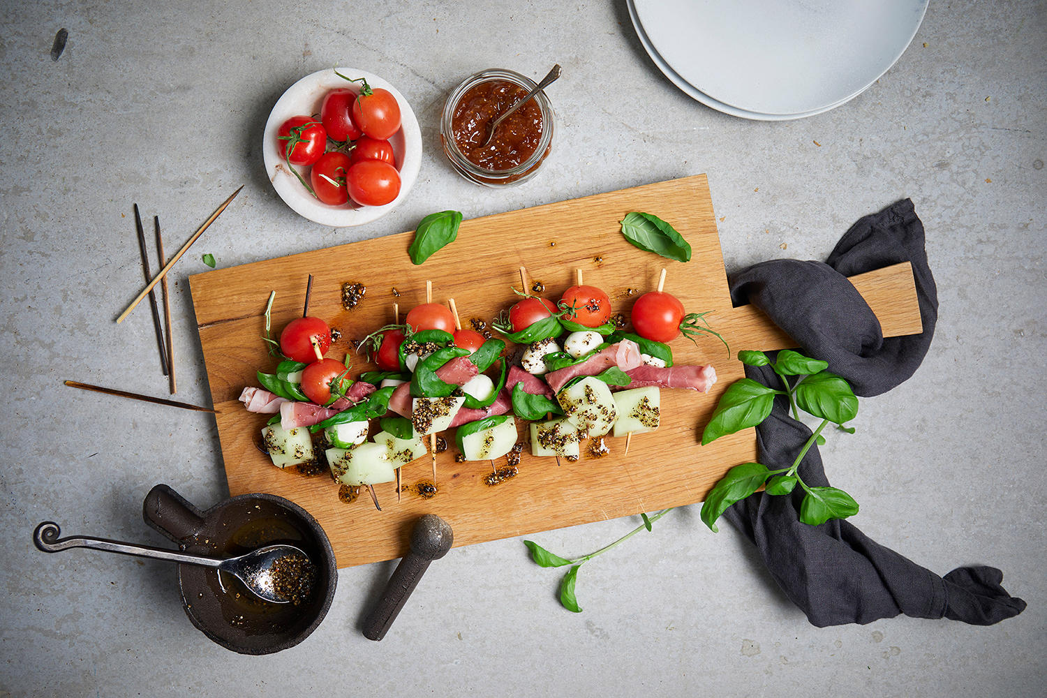 Tapas spidd med spekeskinke, melon og mozzarella servert på lys trefjøl med cherrytomater, frisk basilikum og en hjemmelaget honning-soyasaus med knust pepper.