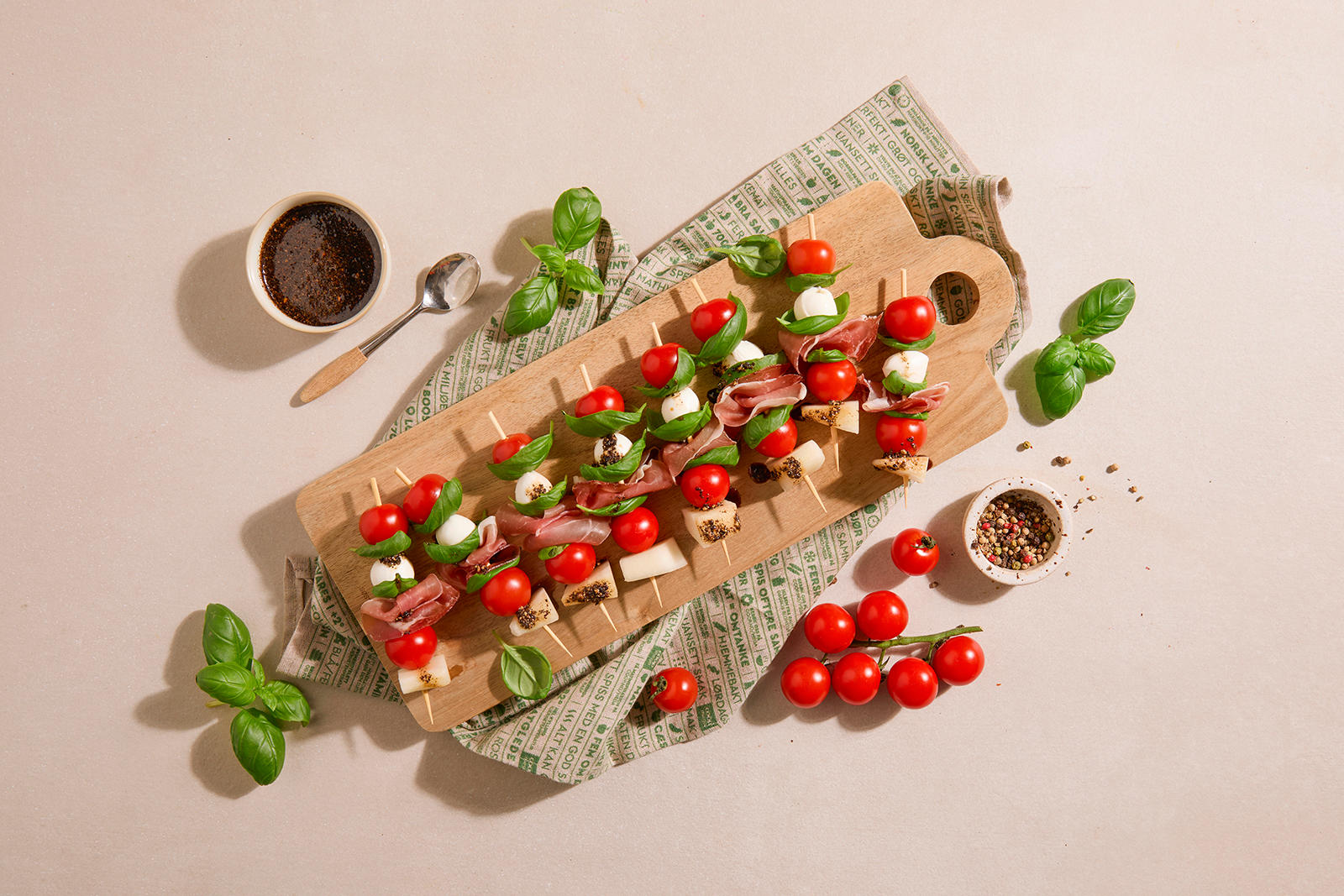 Tapas spidd med spekeskinke, melon og mozzarella servert på lys trefjøl med cherrytomater, frisk basilikum og en hjemmelaget honning-soyasaus med knust pepper.
