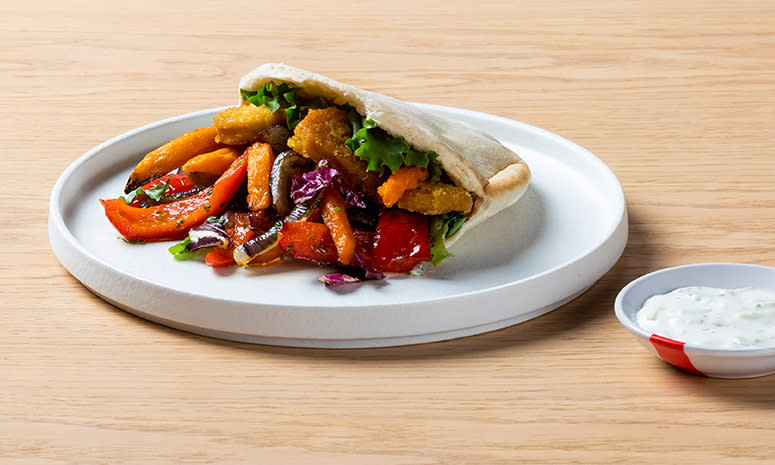 Vegetarnuggets i pita med grønnsaker, servert på en hvit tallerken med høy kant og en liten skål med tzatziki på høyre siden av tallerkenen