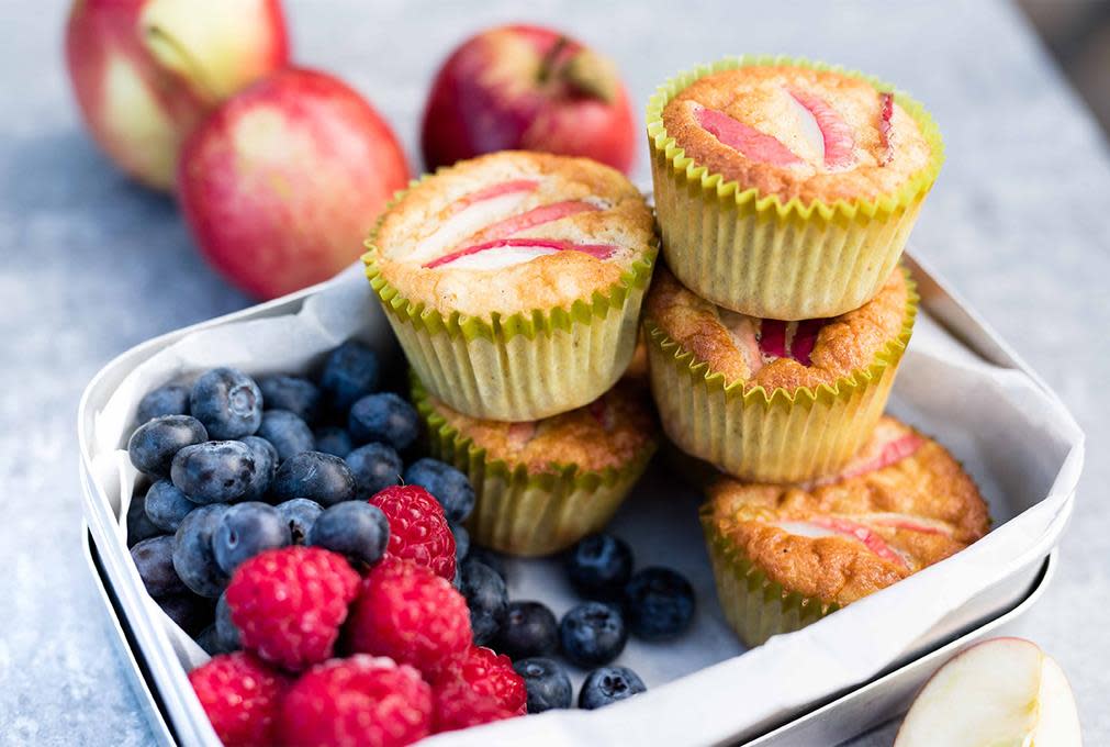 Grove eplemuffins pyntet med epleskiver før steking, servert i matboks med friske bringebær og blåbær.