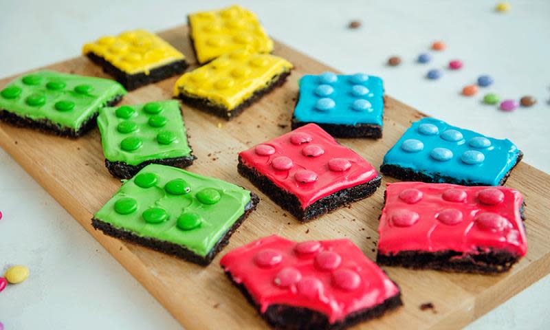 Lego-brownies med kremostglasur i forskjellige farger, servert på trefjøl. Browniene har fargede nonstop på toppen av glasuren så de ser ut som legoklosser.