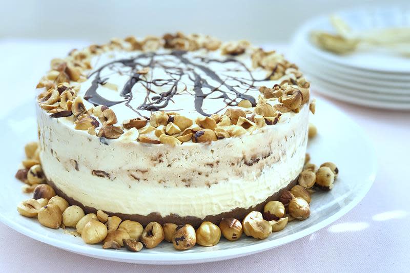 Rund iskake med karamell, hasselnøtter og sjokoladesaus servert på hvitt fat, og pyntet med nøtter og mer sjokoladesaus.