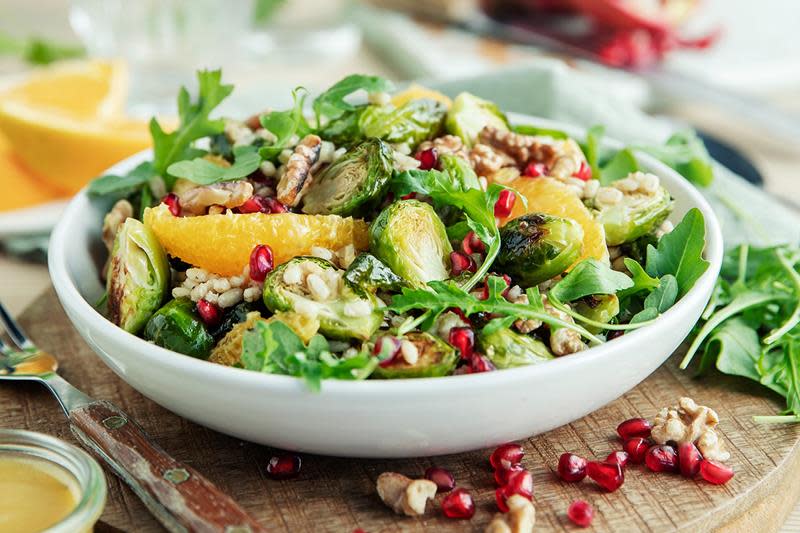 Fargerik rosenkålsalat med gyldne appelsinskiver, røde granateplefrø og fyldig sennepsdressing. Servert i lys skål på trefat.