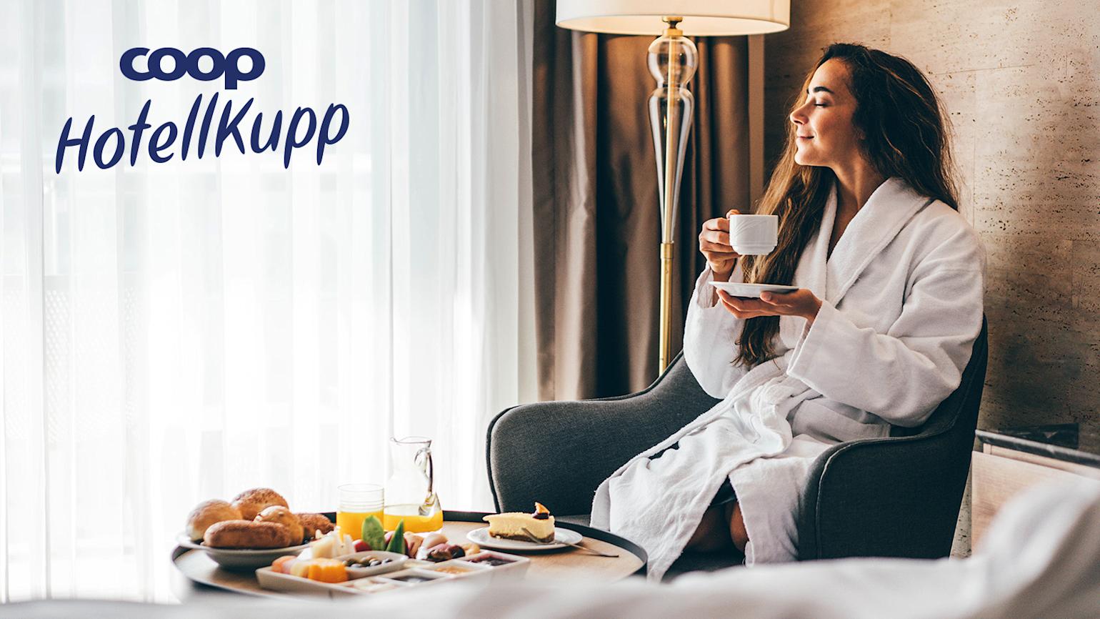 en dame sitter i et fint hotellrom og nyter kaffe i en stol ved siden av sengen