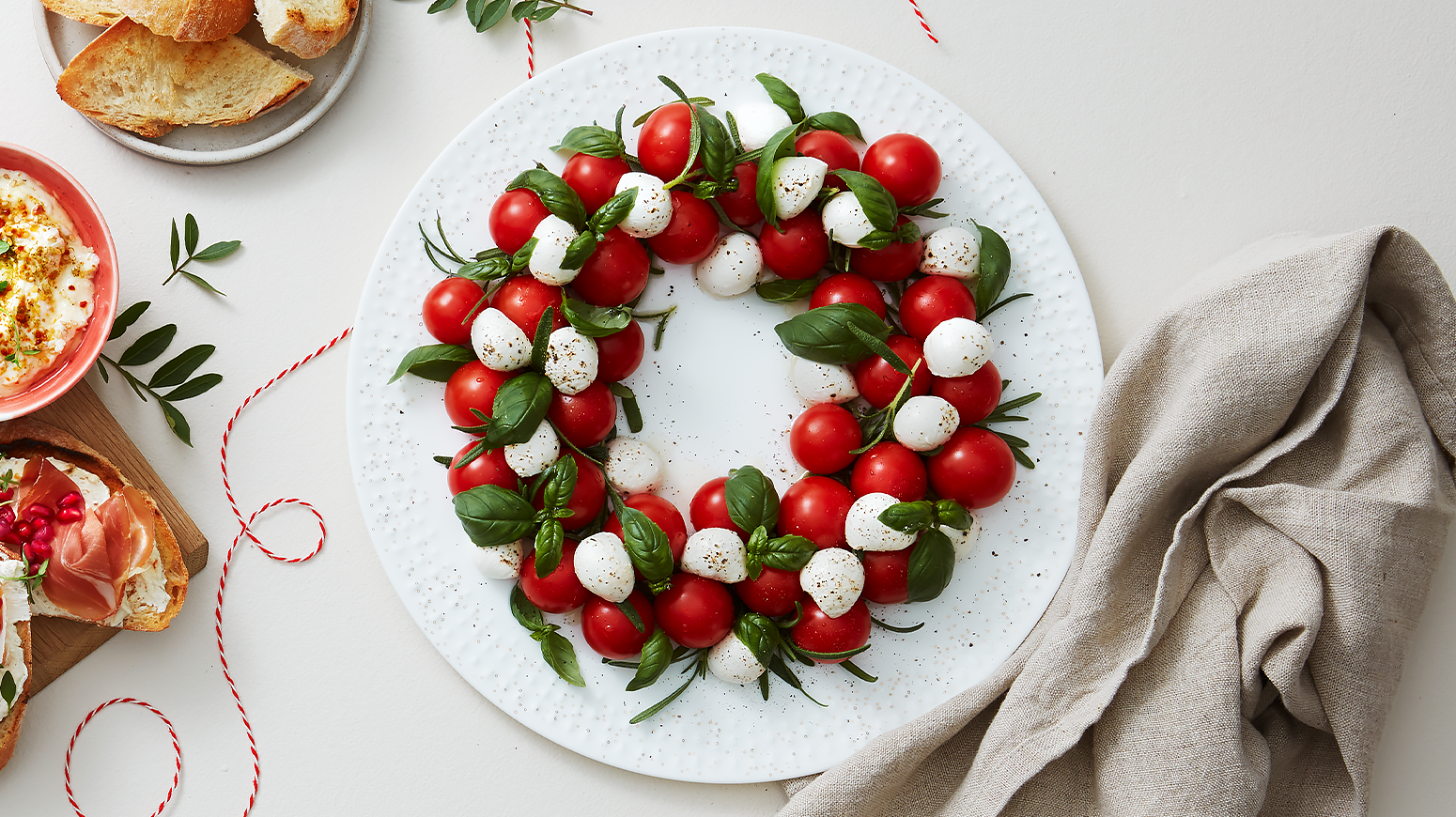 Caprese-krans av cherrytomater, mozzarellakuler og fersk basilikum servert på hvit tallerken.