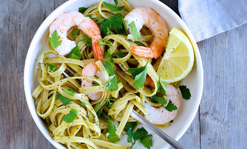 Fullkornspasta i form av tagliatelle, med pesto og scampi, overstrødd med fersk bladpersille. Sitronbåt på siden.