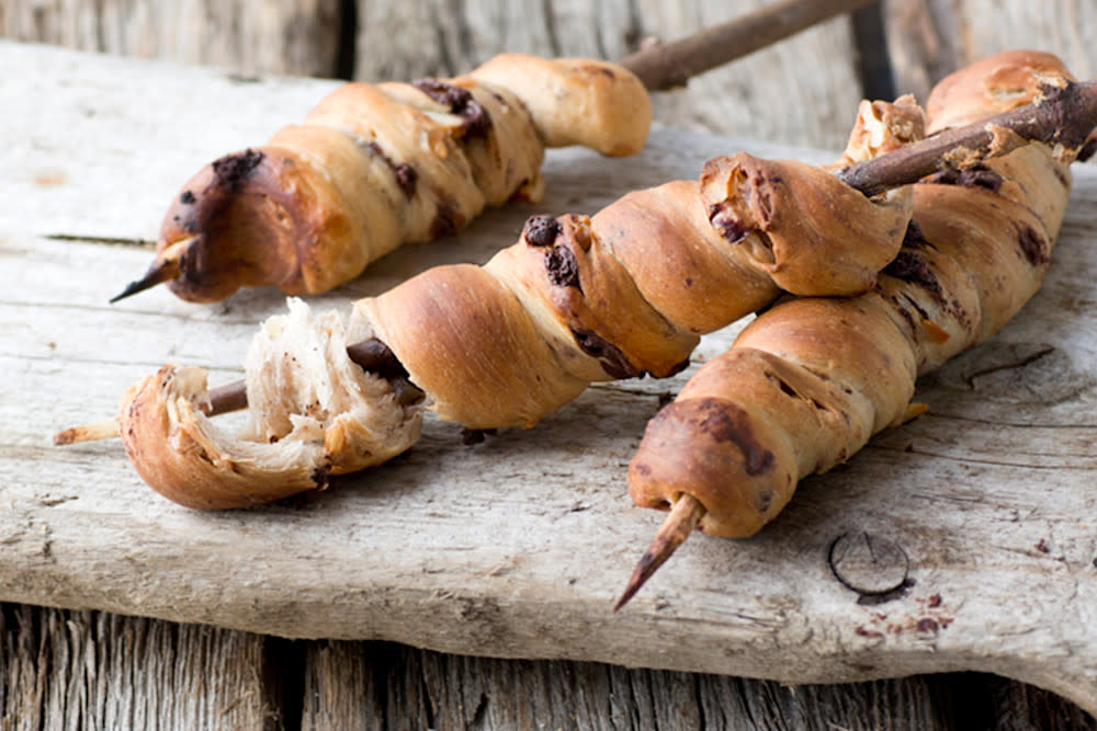 Pinnebrød med sjokolade grillet på pinne, servert på rustikk trefjøl på trebord.