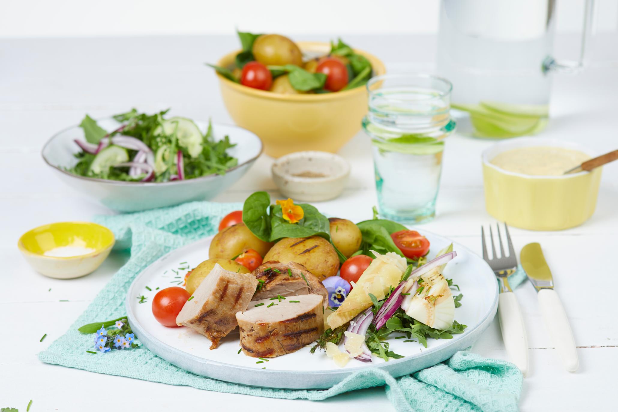 Indrefilet av svin med grønn salat og grillet fennikel, poteter og bearnaise på en hvit tallerken foran en hvit skål med salat, en gul skål med poteter og en gul skål med saus
