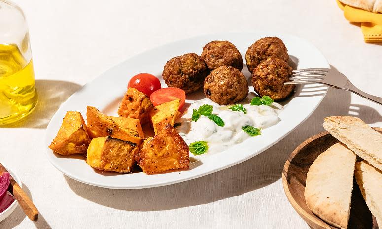 Pita med falafel, søtpotet og hjemmelaget tzatziki. Falafel, søtpotet og tzatziki servert på oval hvit tallerken med ferske tomater. Pitabrød i treskål ved siden av.