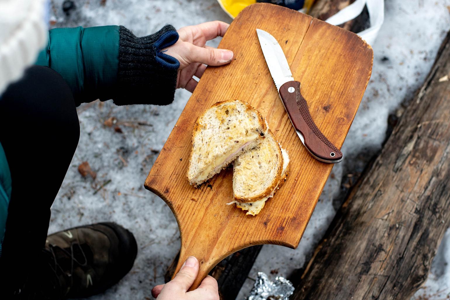 Toast laget på bål, delt i to og servert på trefjøl. Snø og tømmerstokk i bakgrunnen.