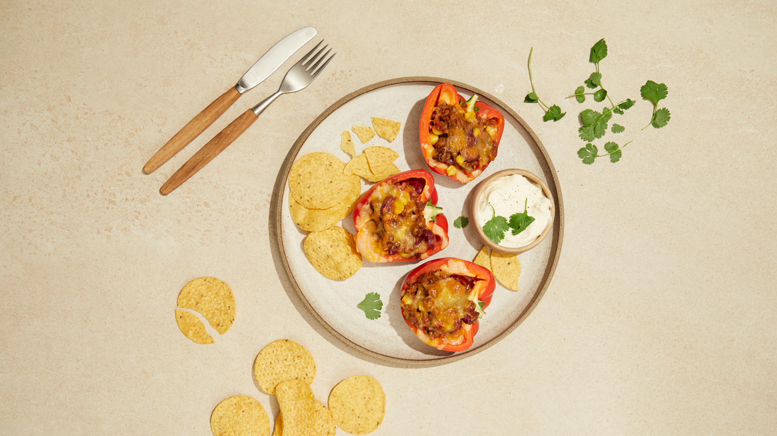 Fylt tacopaprika, rød paprika med tacofyll av kjøttdeig og ost, servert på hvit tallerken med nachochips og rømme.