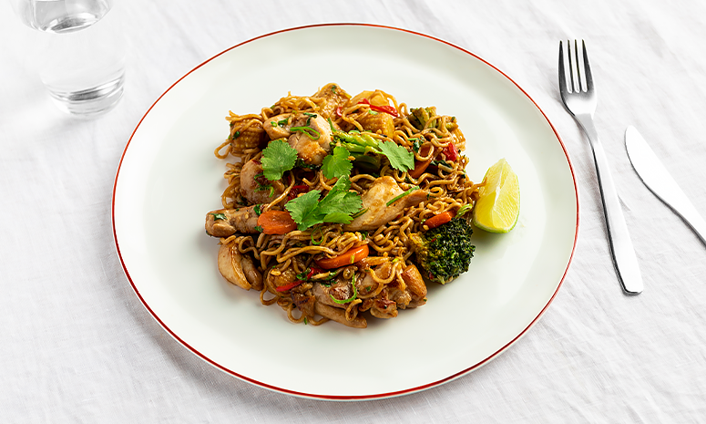 Kyllingwok og en limebåt på en hvit tallerken med rød kant.