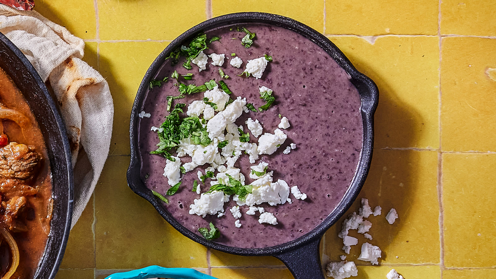 Refried beans servert i støpejernspanne, og pyntet med fetaost og hakket koriander på toppen.