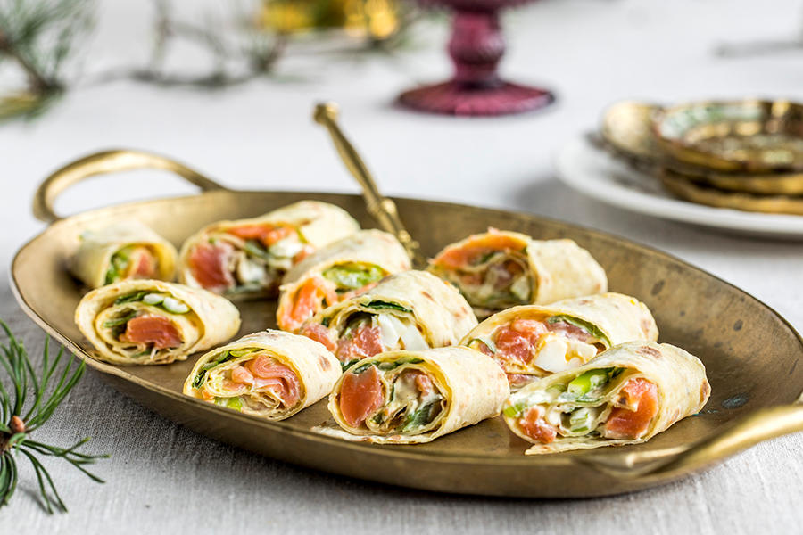 Rakfiskruller med egg og vårløk servert på messingfat, på juledekket bord med hvit duk.