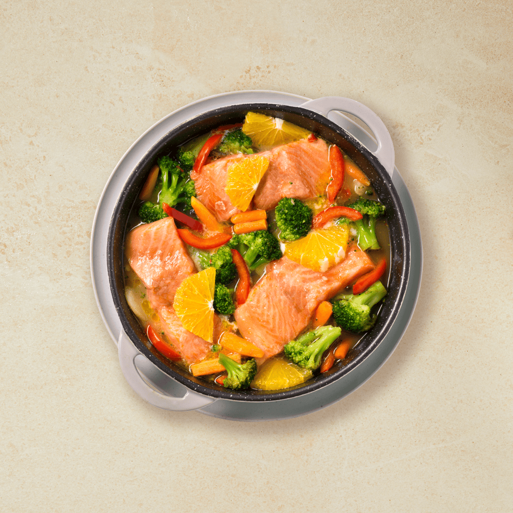 Ovnsbakt ørret med appelsin og wokgrønnsaker servert i grå ildfast form på hvit bakgrunn.