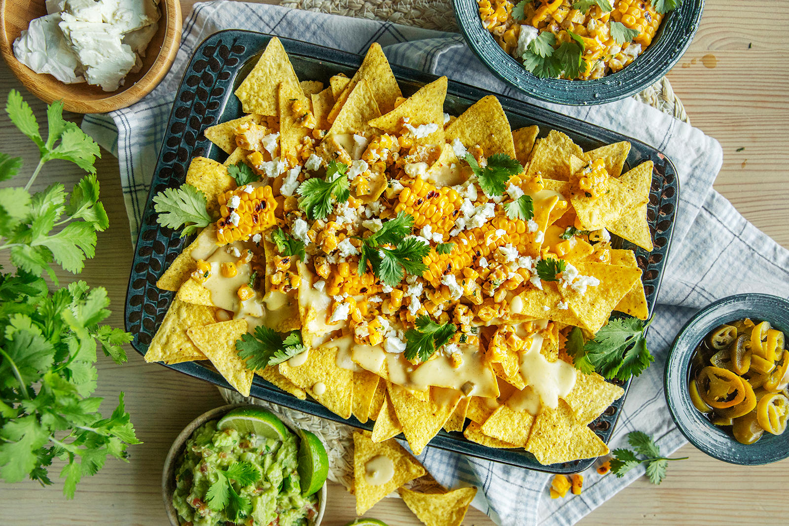 Vegetarnachos med ostesaus og mais i langpanne. Guacamole, grillet mais, jalapenos og koriander på siden.