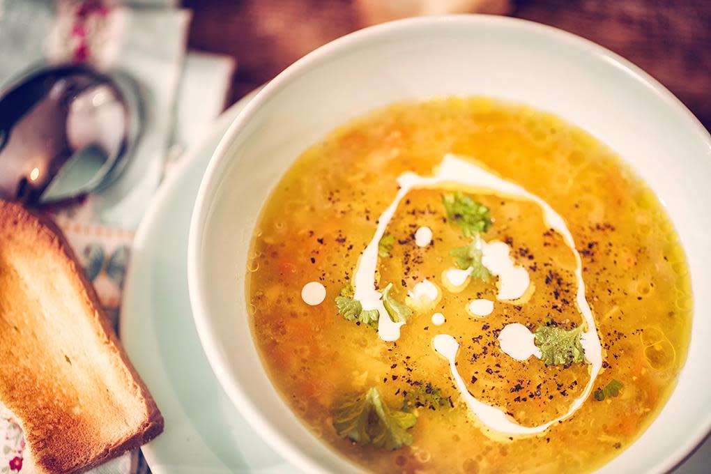 Gul suppe i hvit skål, med fløte ringlet i, og urter på toppen. Toast på siden.