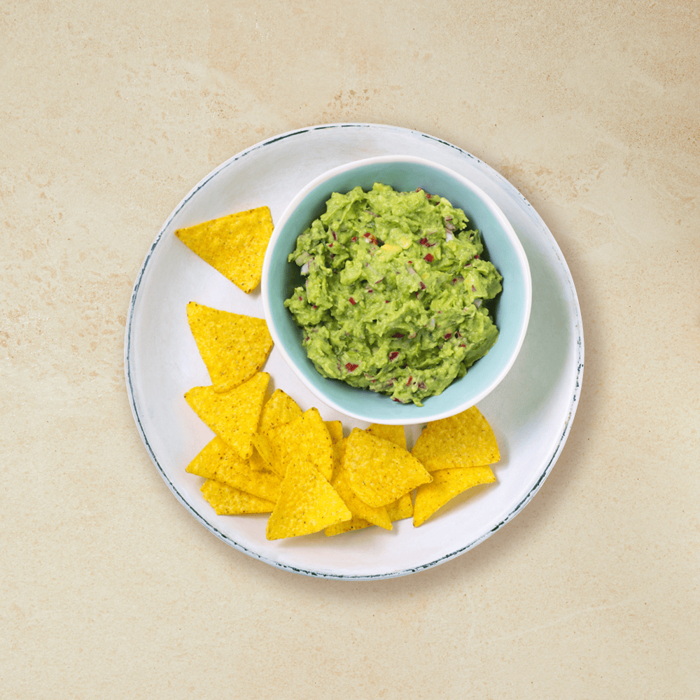 Guacamole i en bolle på tallerken med tortilla chips
