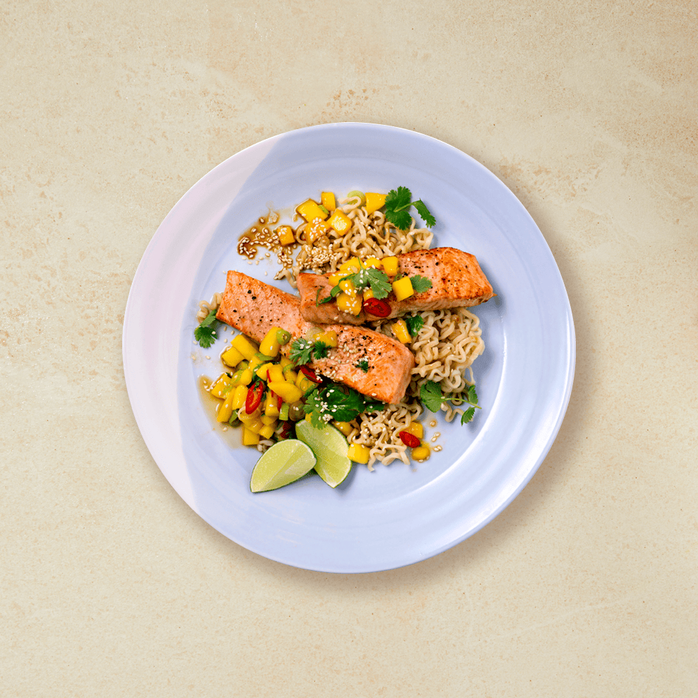 Laks med mangosalat og nudler servert med limebåter på en lys lilla tallerken