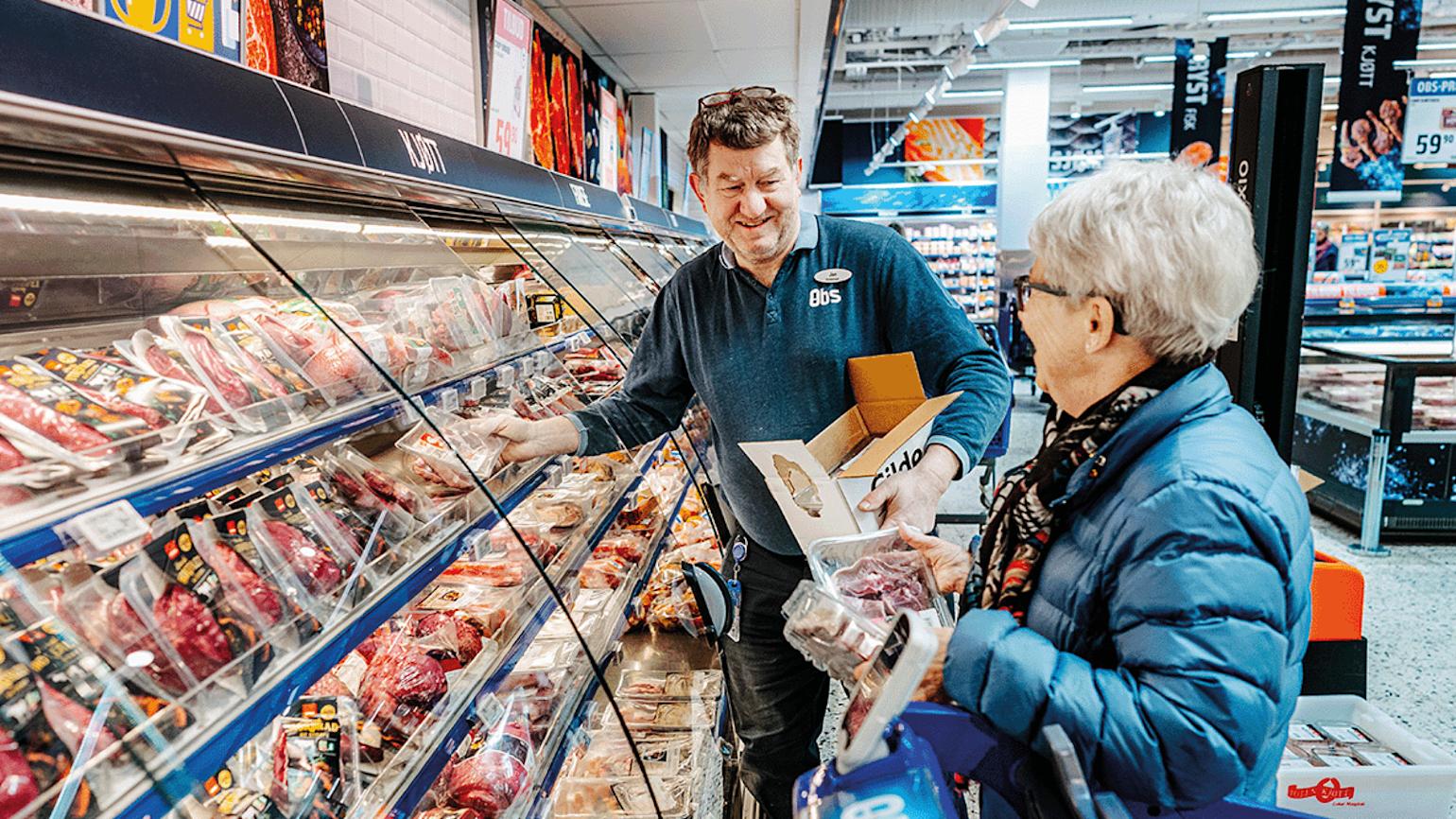 Mann pakker ut kjøttvarer og snakker med eldre dame.