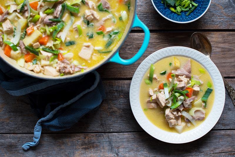 Gylden hønsefrikassé med grønnsaker, servert i turkis støpejernskjele, på rustikk trebakgrunn.