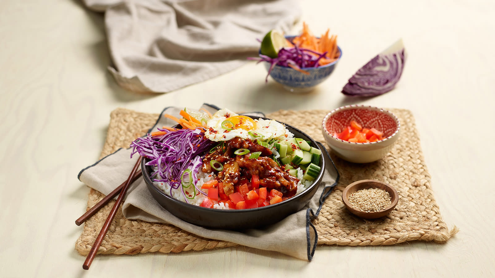 Koreansk BBQ bowl med egg servert med spisepinner på flettet underlag.