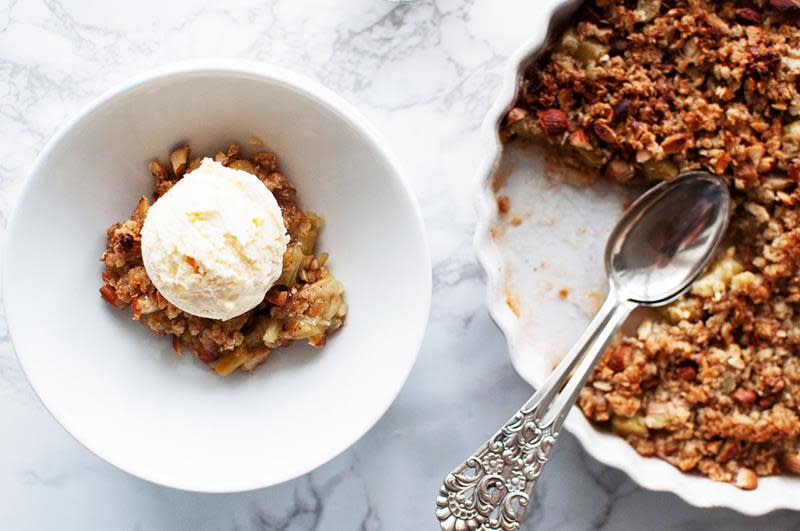 Gyllen rabarbrapai med smuldretopping, servert i en hvit paiform på hvit marmorbakgrunn. Hvit skål med en porsjon rabarbrapai med en kule vaniljeis på toppen.