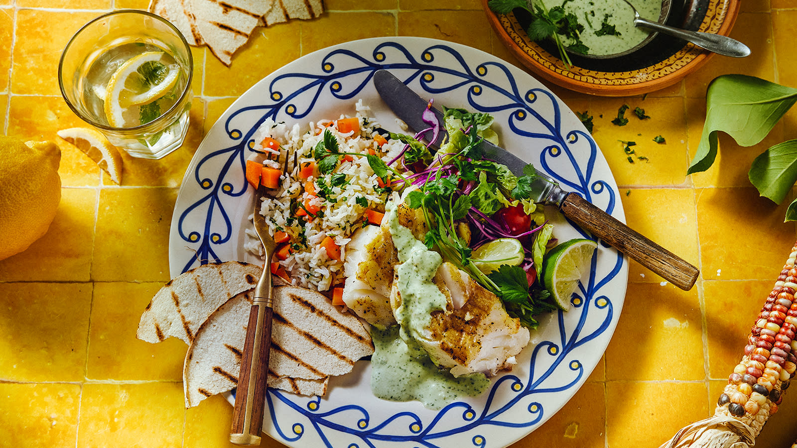 Torsk med meksikansk ris og koriandersaus servert på blåmønstret asjett med grillet flatbrød, urter og en frisk salat.