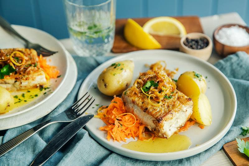 Seibiff med smeltet smør, råkost, gylden stekt løk og poteter med et dryss persille. Servert på lys tallerken, med sitronbåter, salt og pepper på siden.