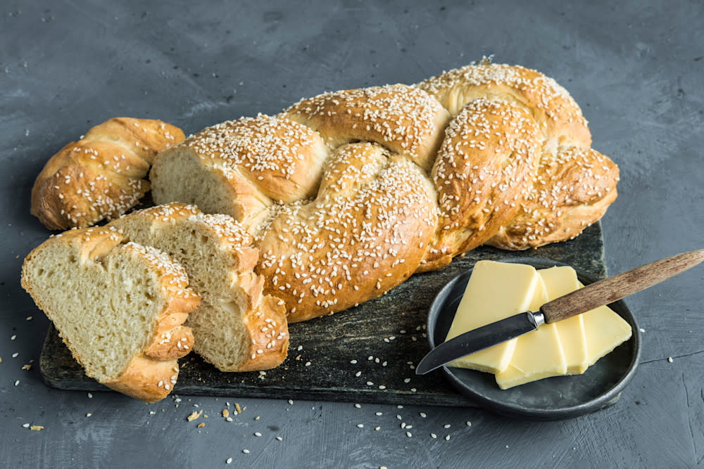 Brioche - verdens beste loff, pyntet med sesamfrø og servert hel og i skiver på mørk trefjøl med en skål smør ved siden av.