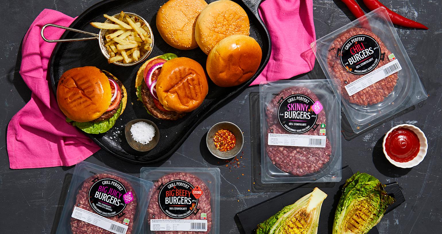 Grill Perfekt burgere i emballasje på mørk steinbakgrunn, samt tilberedte burgere i burgerbrød på svart serveringsfat. Grillet hjertesalat, og små skåler med tilbehør på siden.