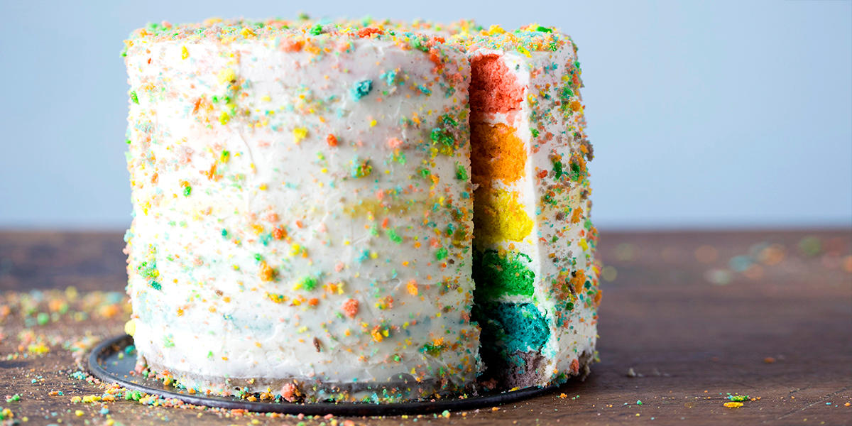 Regnbuekake med kremostfrosting. Kaken er laget i seks lag, der hvert av lagene har ett av regnbuens farger. Hvit frosting utenpå, med fargerike kakesmuler.