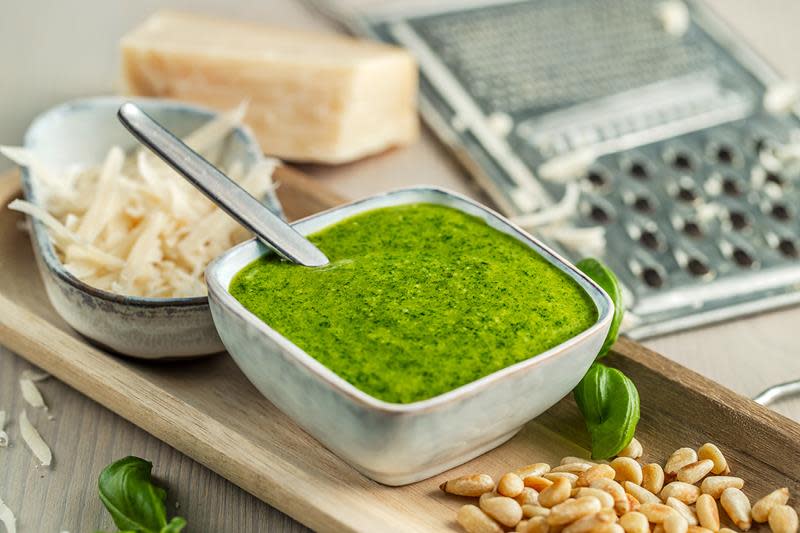 Hjemmelaget grønn pesto i firkantet skål, servert på avlangt trebrett med skivet parmesan, ristede pinjekjerner og fersk basilikum.