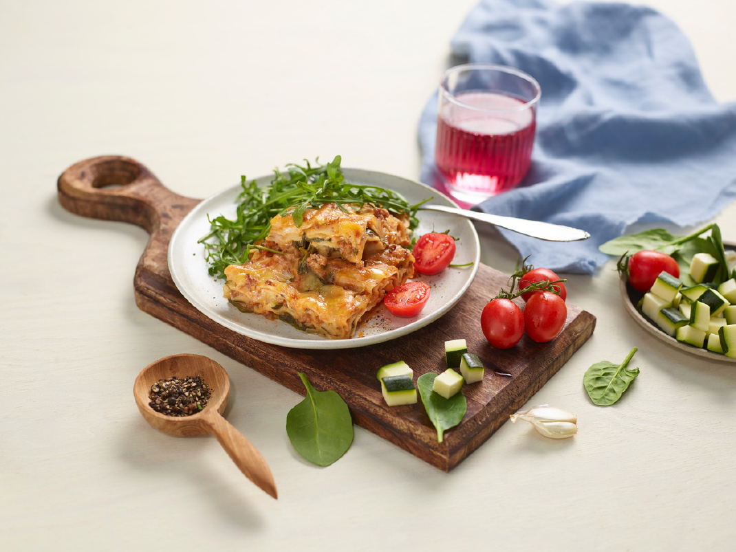 Lasagne på en tallerken som står oppå en fjøl med oppkuttet squash og hele tillater rundt seg