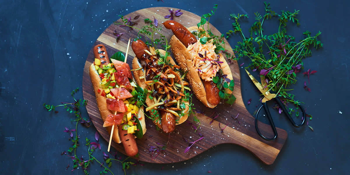 Tre gode pølsetoppinger. Tre grillpølser med forskjellige toppinger; karrimajones og mangosalsa, sprø grønnsaksticks og chilimayo med lobnobs.