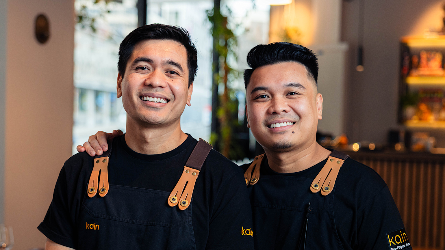 To manlige kokker står i en restaurant og smiler til kamera