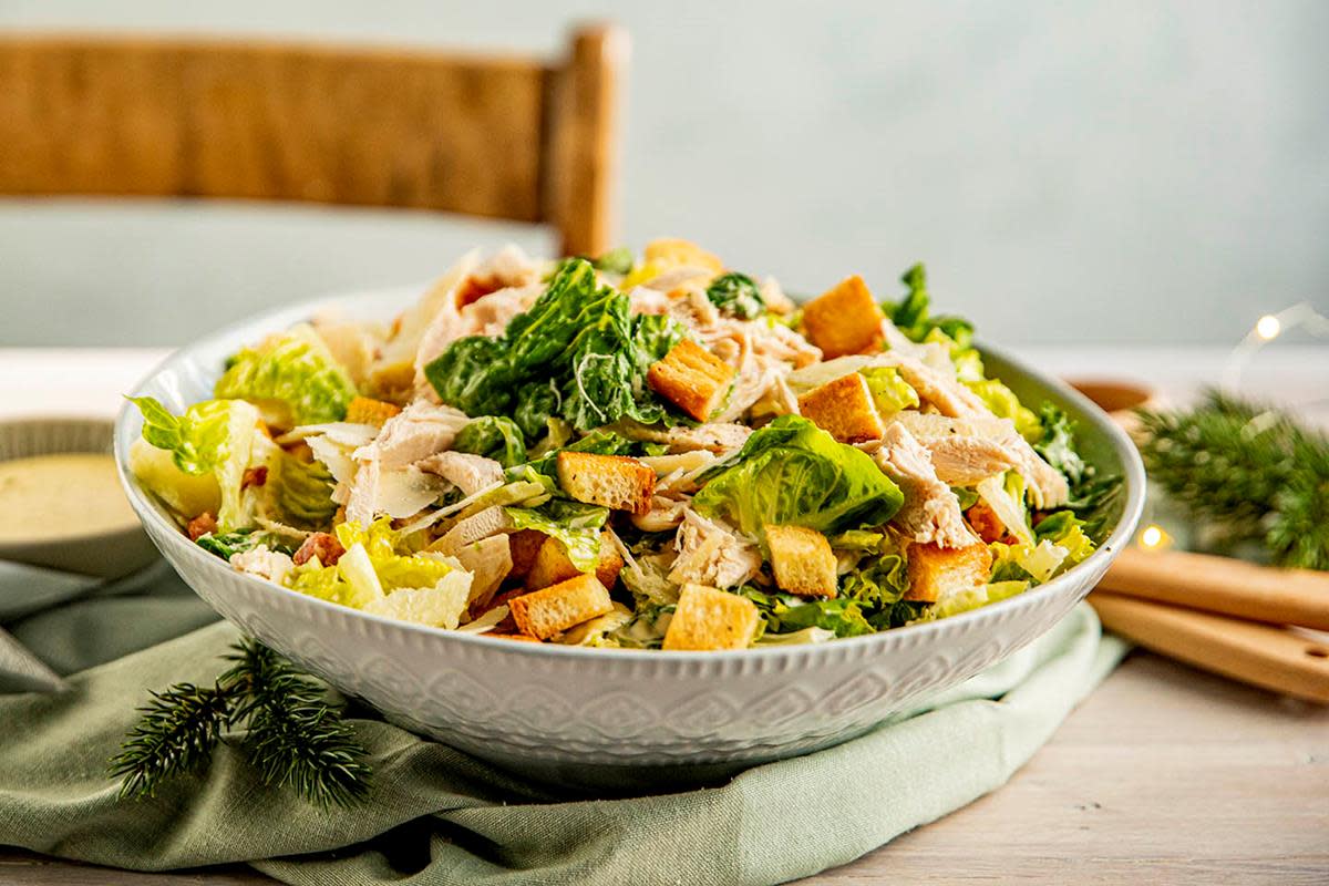 Frisk grønn cæsarsalat med hjertesalat, bacon, hjemmelagede krutonger og rester av kalkun. Hjemmelaget cæsardressing på siden. Hint av jul i bakgrunnen.