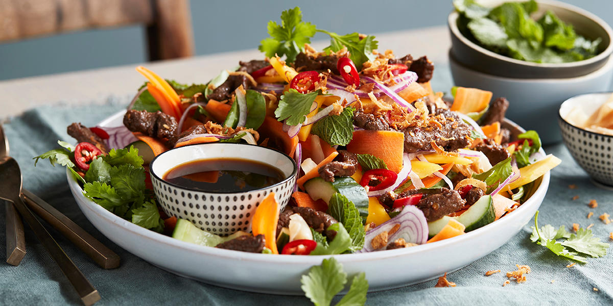 Lettvint biffsalat med herlige asiatiske smaker, lagt på dyp asjett med fargerike grønnsaker, friske urter og en skål dipsaus.