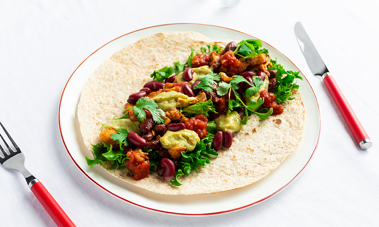 Taco med kylling og bønner i tortillalefse på en hvit tallerken.