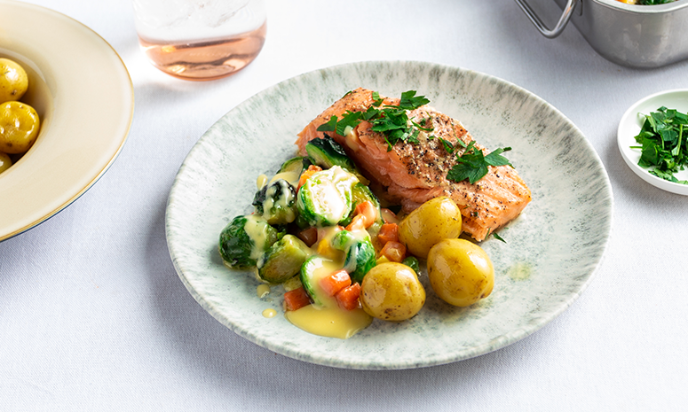 Ovnsbakt laks med sandefjordsmør og grønnsaker, servert på lys tallerken på dekket middagsbord.