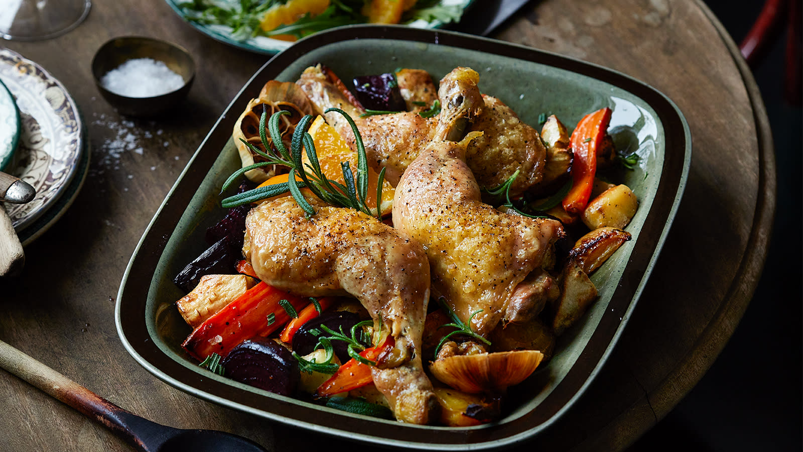 Kyllinglår med ovnsbakte grønnsaker servert i grønn ildfast form på mørkt rustikk bord.