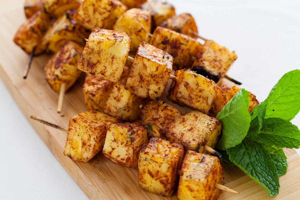 Grillet ananas med kanel og sukker, skåret i biter og tredd på trespyd. Servert på trefjøl, med en kvist mynte.