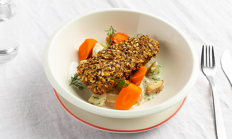 Frøbakt fisk over gulrøtter, poteter og hvit saus i hvit skål.